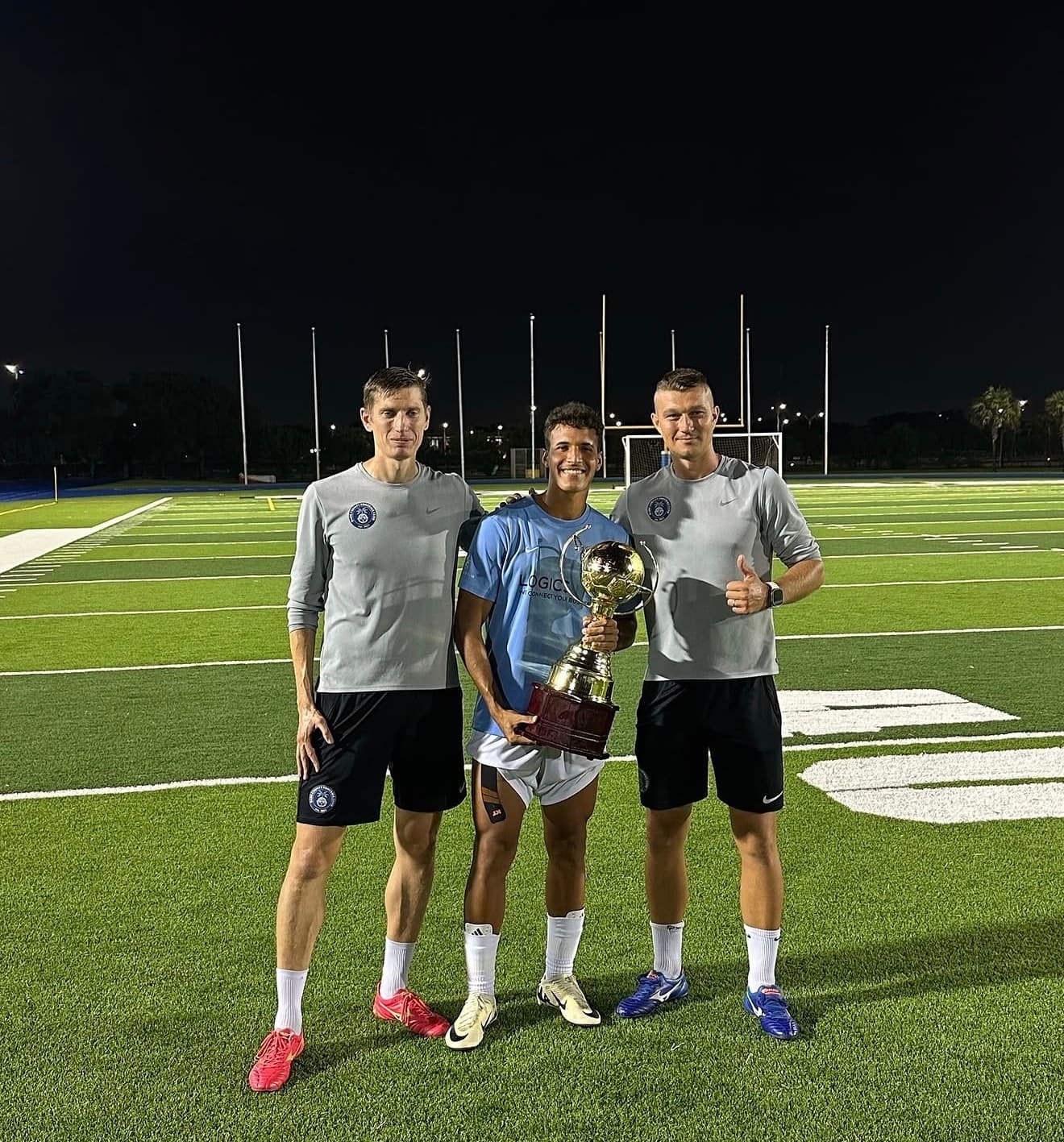 Dade County FC coaches and player with a trophy on the pitch